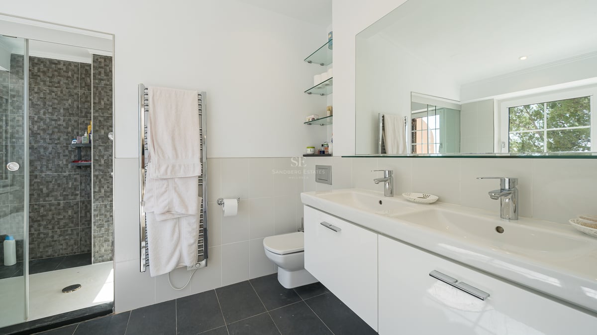 Salle de bain moderne avec double vasque blanche, grand miroir, sèche-serviettes et douche à l'italienne.