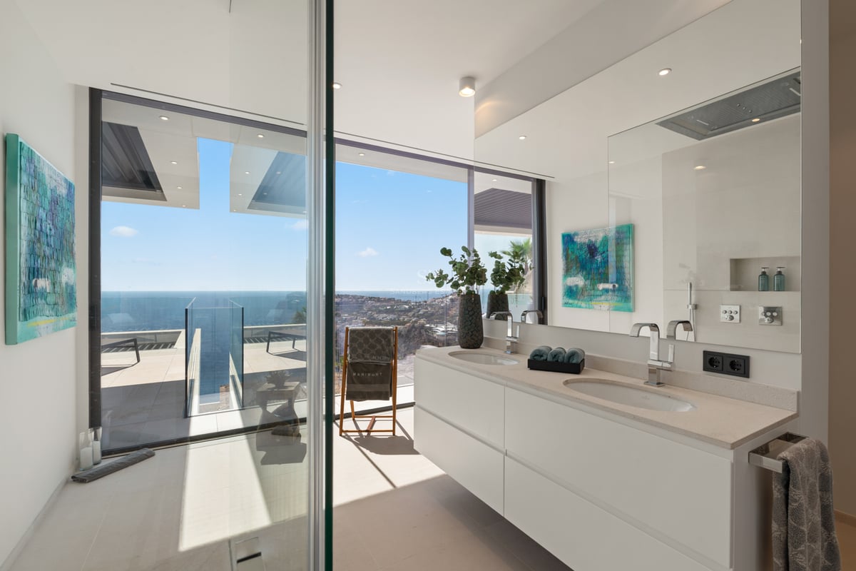 Salle de bain moderne avec double vasque blanche et grandes baies vitrées offrant une vue sur la Méditerranée.