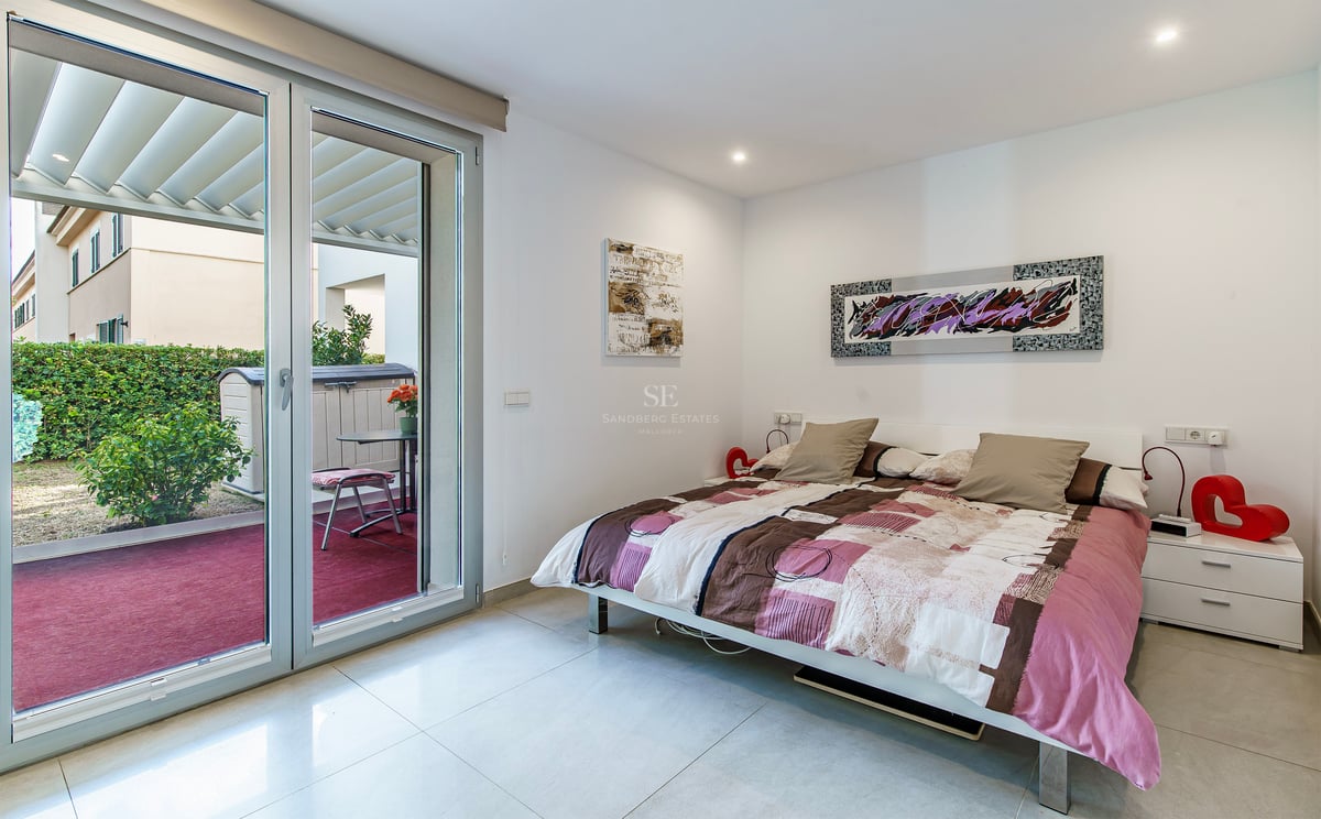 Chambre lumineuse avec un lit double, de l'art moderne et une grande porte vitrée coulissante ouvrant sur une terrasse.