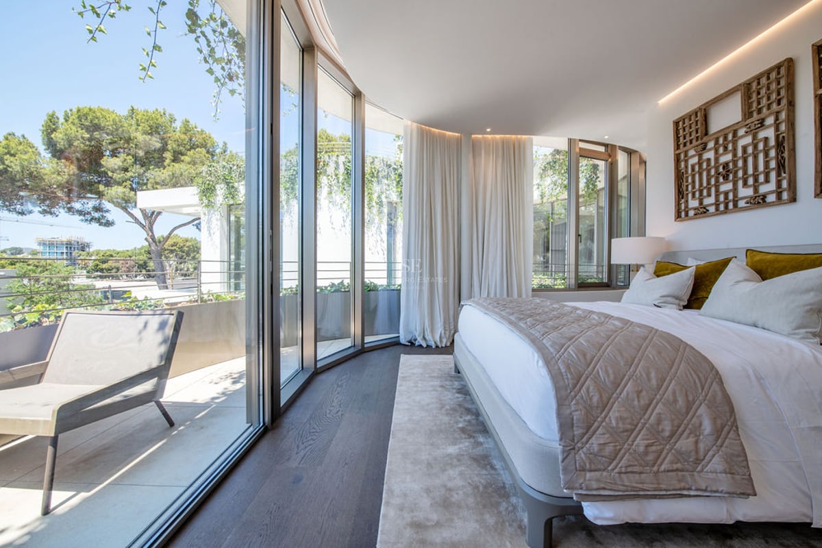 Chambre de maître contemporaine avec murs en verre incurvés, parquet en bois foncé et accès à une terrasse privée.