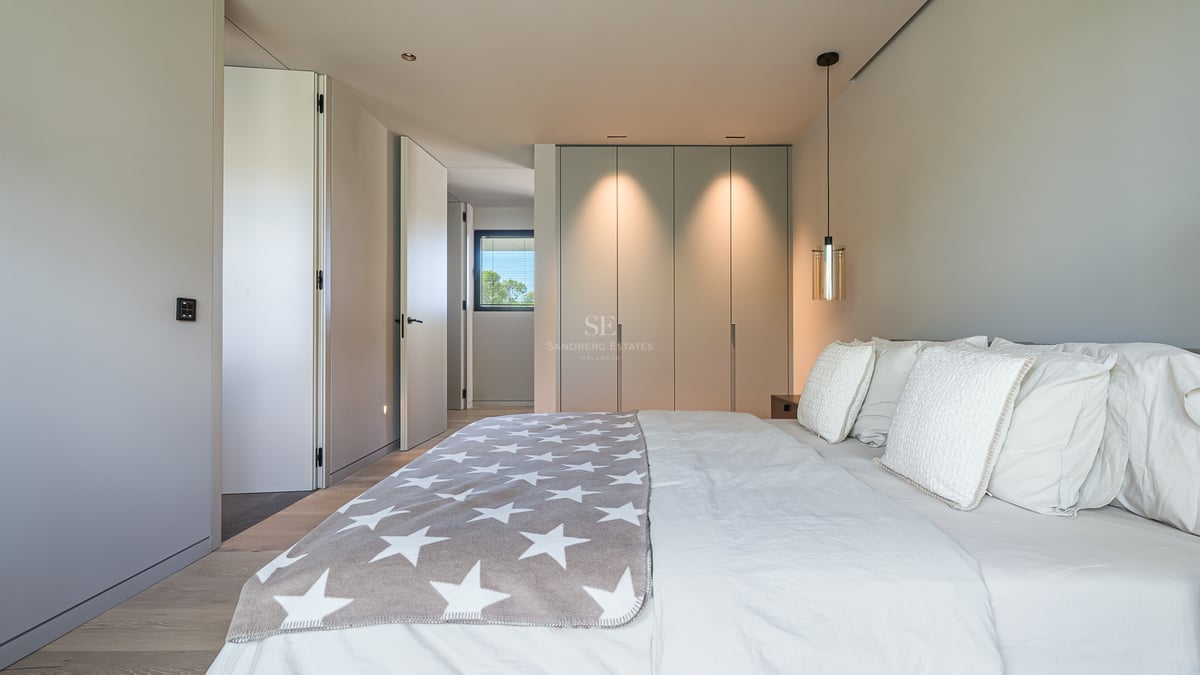 Chambre moderne et lumineuse avec un grand lit, un jeté de lit gris à étoiles et des placards intégrés avec éclairage chaud.