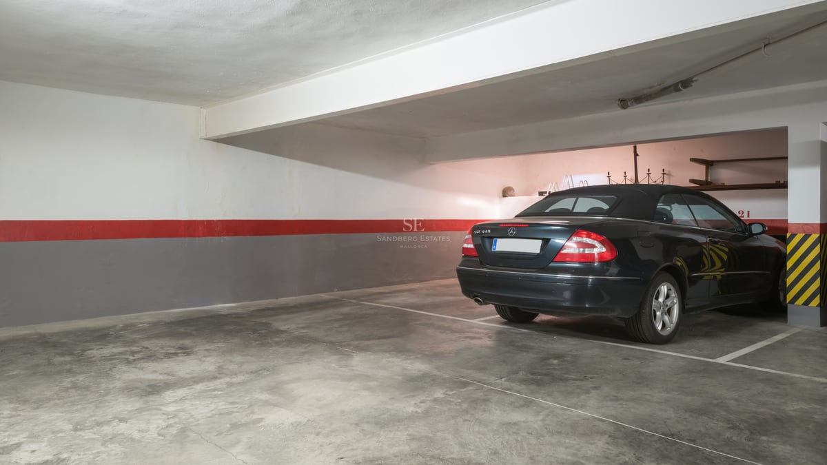 Voiture noire stationnée dans un grand parking souterrain avec sol en béton poli et murs balisés.