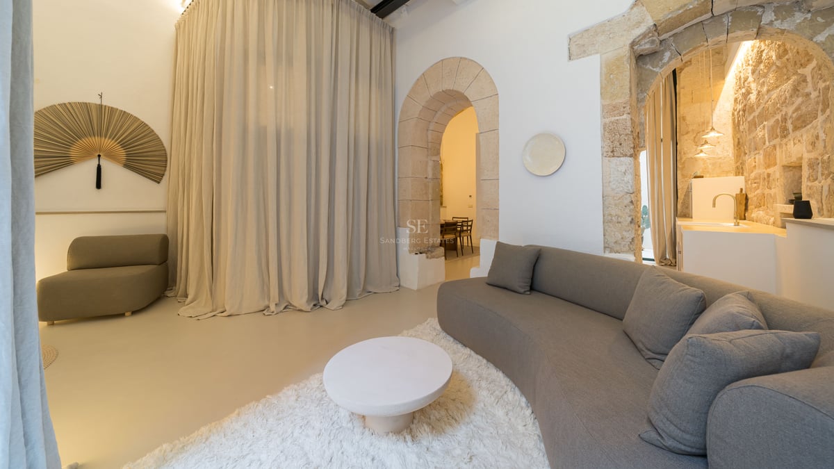 Salon contemporain avec canapé incurvé, arches en pierre, sol en microciment et grands rideaux en lin.