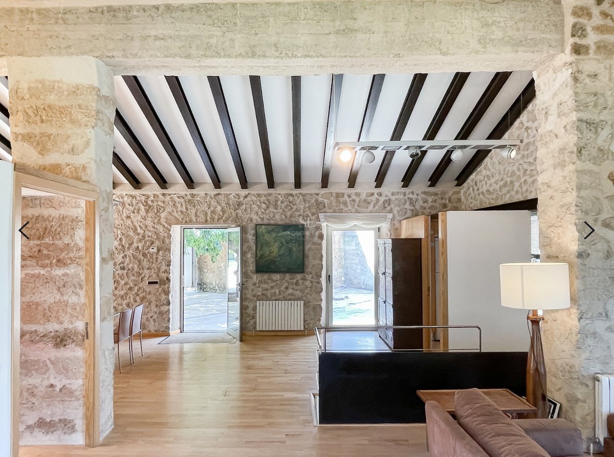 Salon à aire ouverte avec murs en pierre, poutres foncées au plafond et parquet en chêne clair.