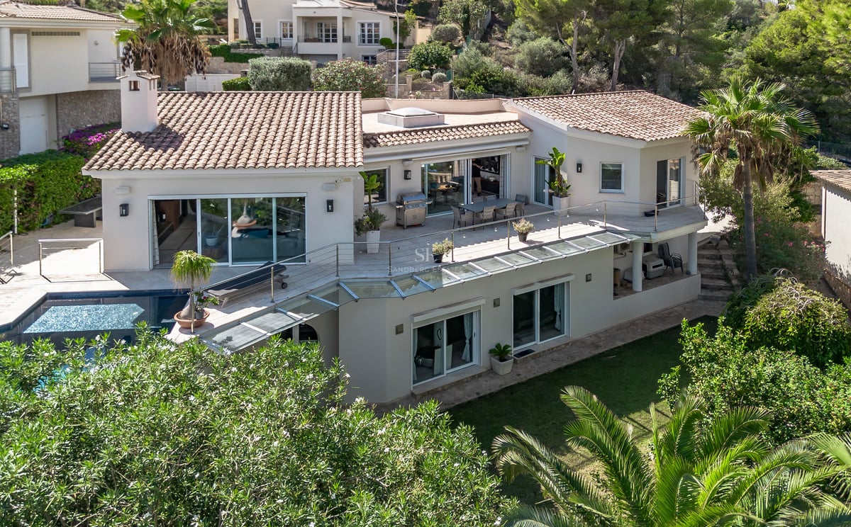 Vue aérienne d'une villa blanche à toit de tuiles, garde-corps en verre, grandes terrasses et piscine privée.