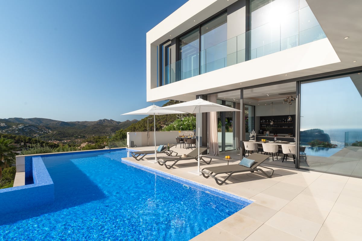 Piscine à débordement de luxe et villa blanche moderne avec vue sur la montagne et chaises longues.