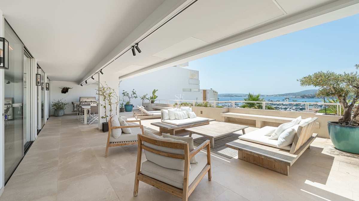 Grande terrasse blanche avec mobilier en bois donnant sur un port de plaisance et la mer Méditerranée.