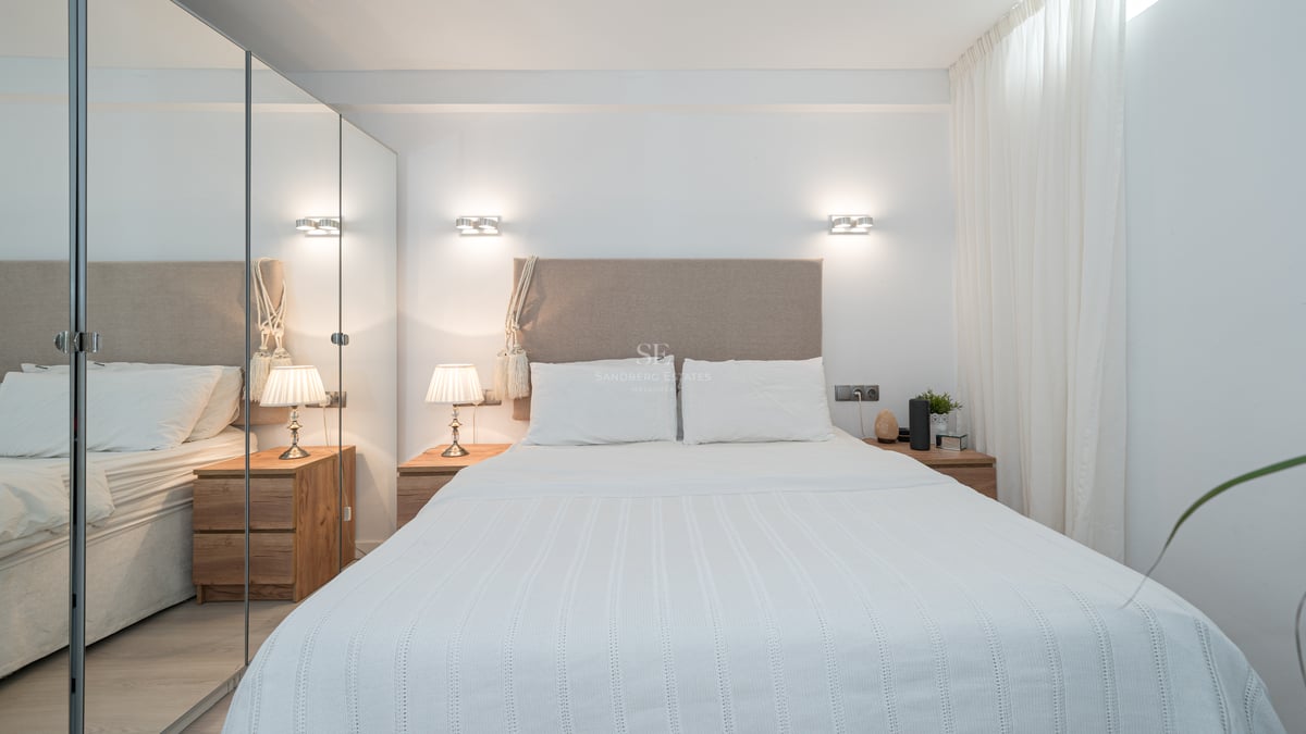 Une chambre moderne et lumineuse avec une tête de lit en beige, du linge blanc et de grands placards à miroirs.
