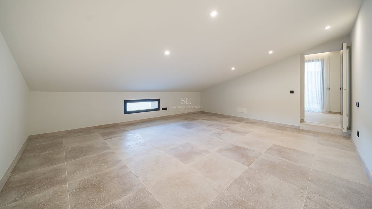 Pièce mansardée vide avec carrelage beige, plafond blanc incliné et spots encastrés.