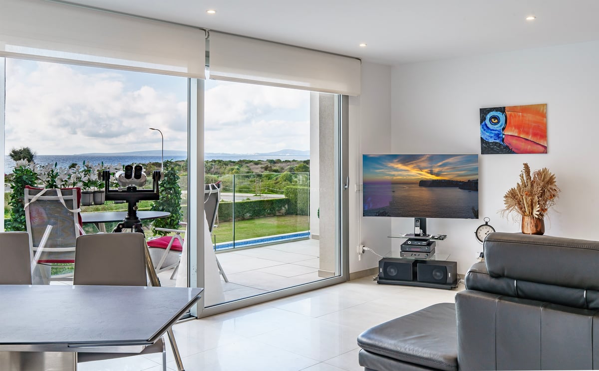 Salon lumineux avec grandes baies vitrées ouvrant sur terrasse avec vue mer, TV et canapé en cuir.