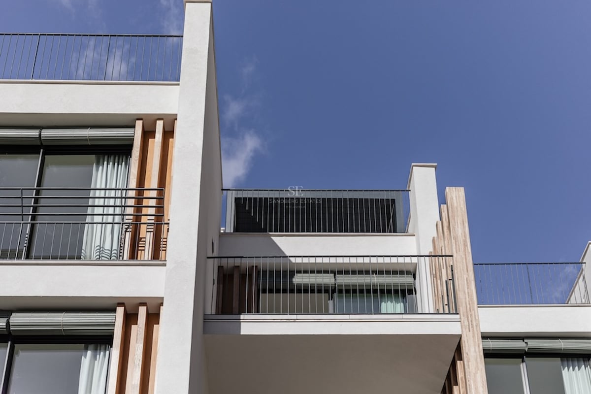 Vue en contre-plongée d'un bâtiment blanc moderne avec des garde-corps en métal et des lattes de bois sous un ciel bleu.