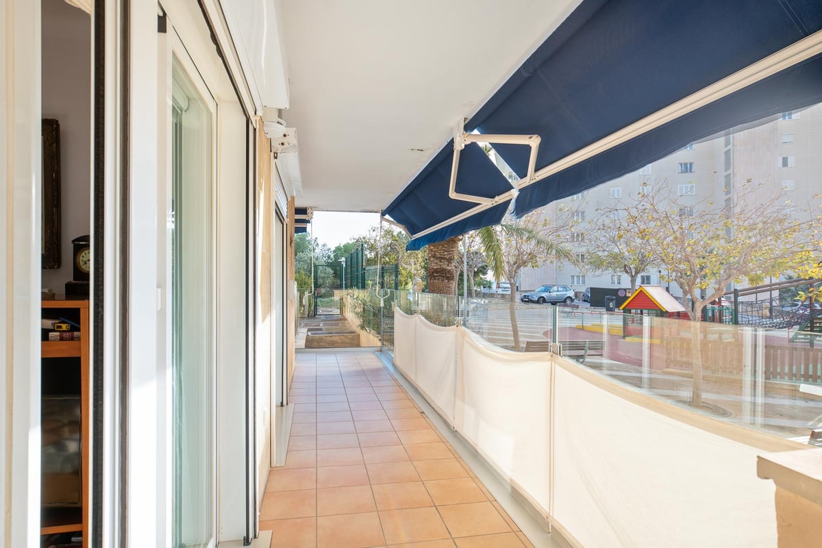 Long balcon avec carrelage en terre cuite, garde-corps en verre et stores bleus escamotables.