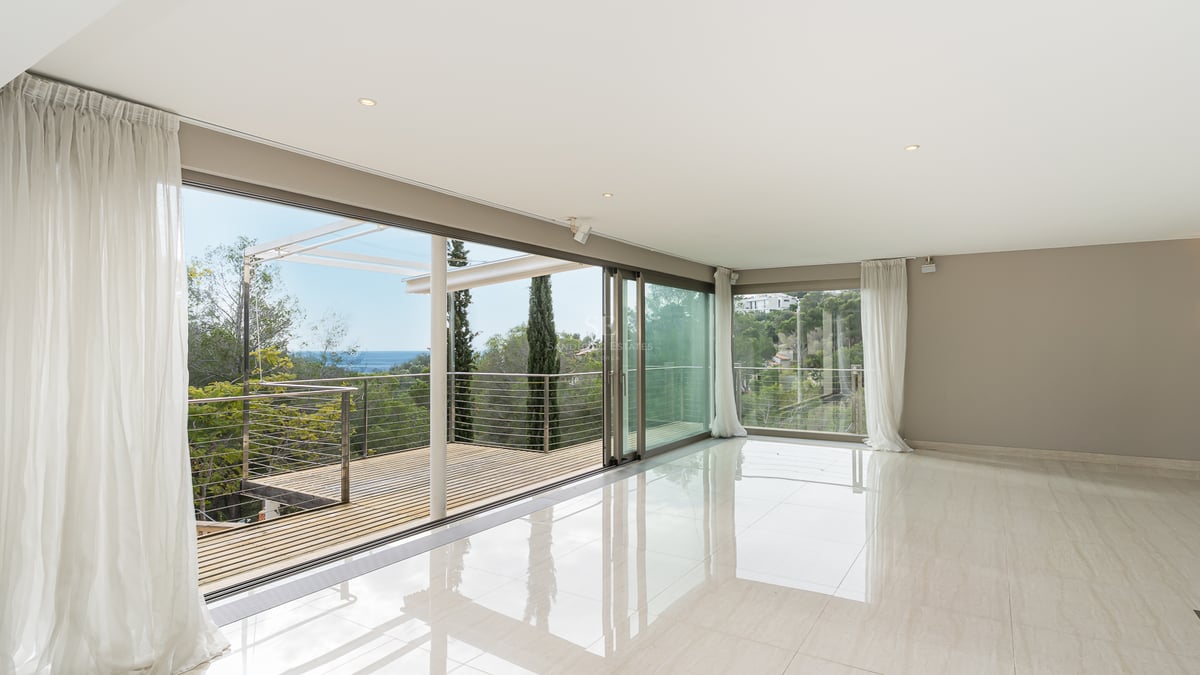 Salon moderne lumineux avec sols polis et baies vitrées coulissantes ouvrant sur une terrasse avec vue mer.