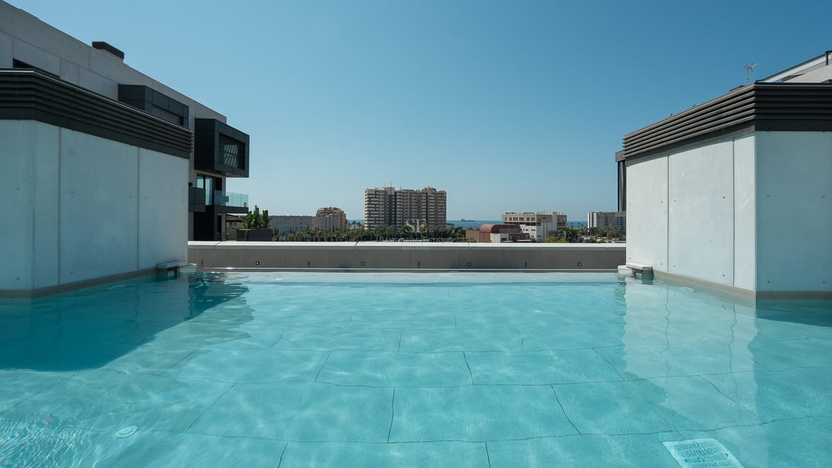 Grande piscine de toit turquoise avec architecture moderne en béton et vue lointaine sur la ville et la mer.