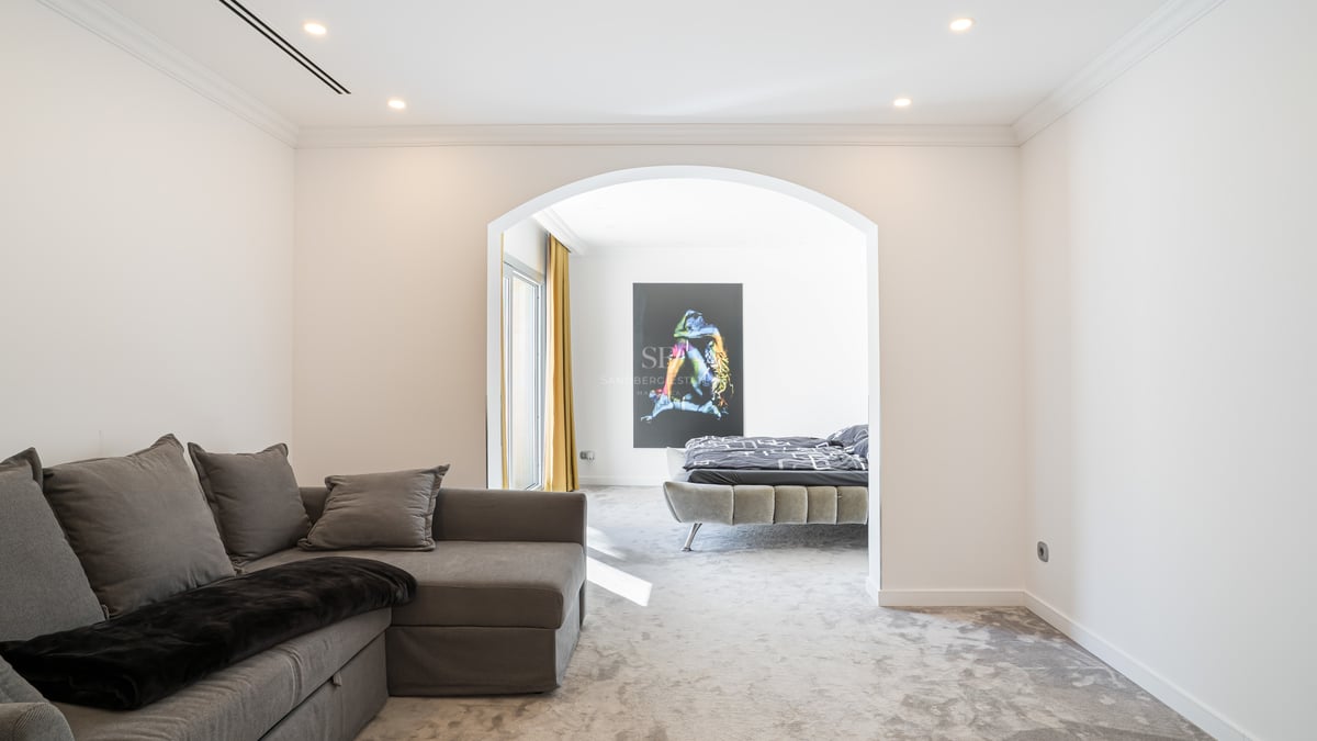 Chambre moderne vue à travers une arche avec lit gris tapissé, moquette épaisse et grande œuvre d'art murale.