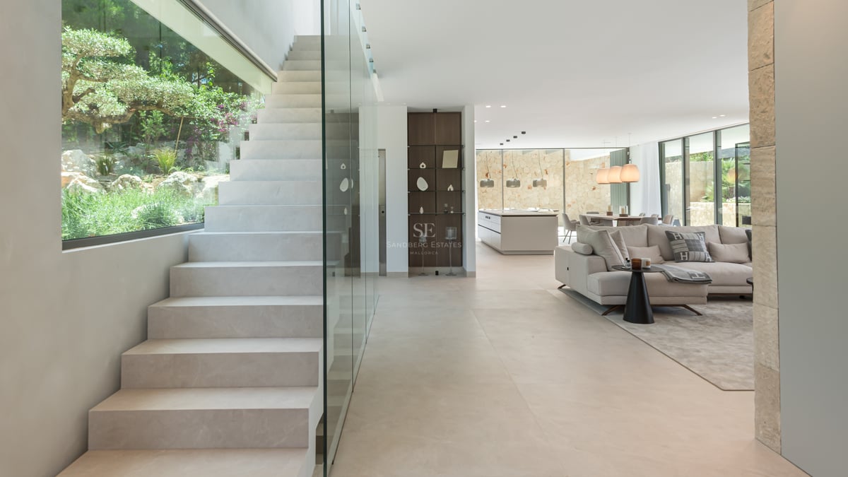 Espace de vie moderne avec escalier en pierre, garde-corps en verre et baies vitrées toute hauteur.