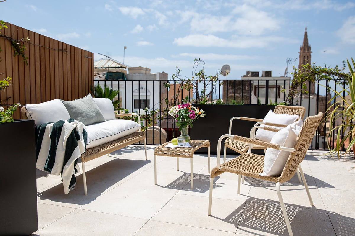 Terraza soleada en azotea con muebles de diseño, suelos de piedra clara y vistas al horizonte histórico de Palma.