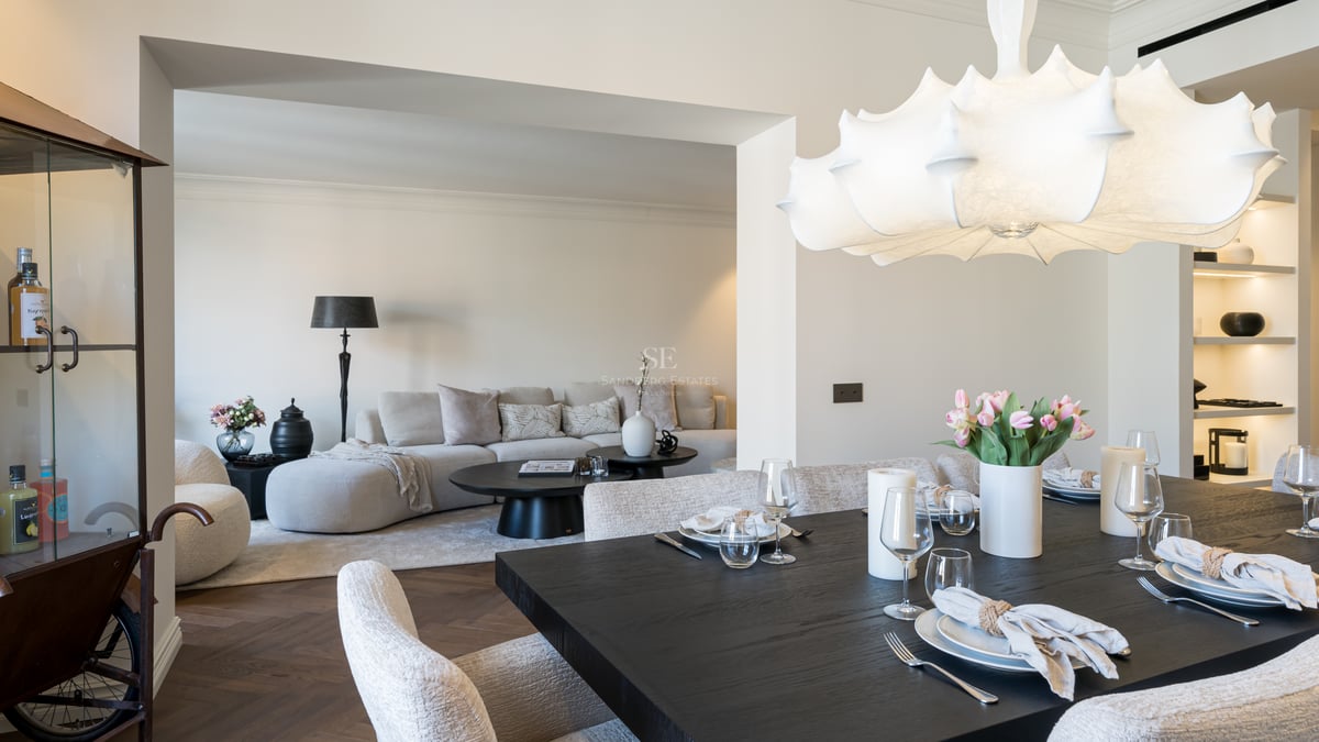 Elegant dark wood dining table set for guests, leading into a bright contemporary living room with herringbone floors.