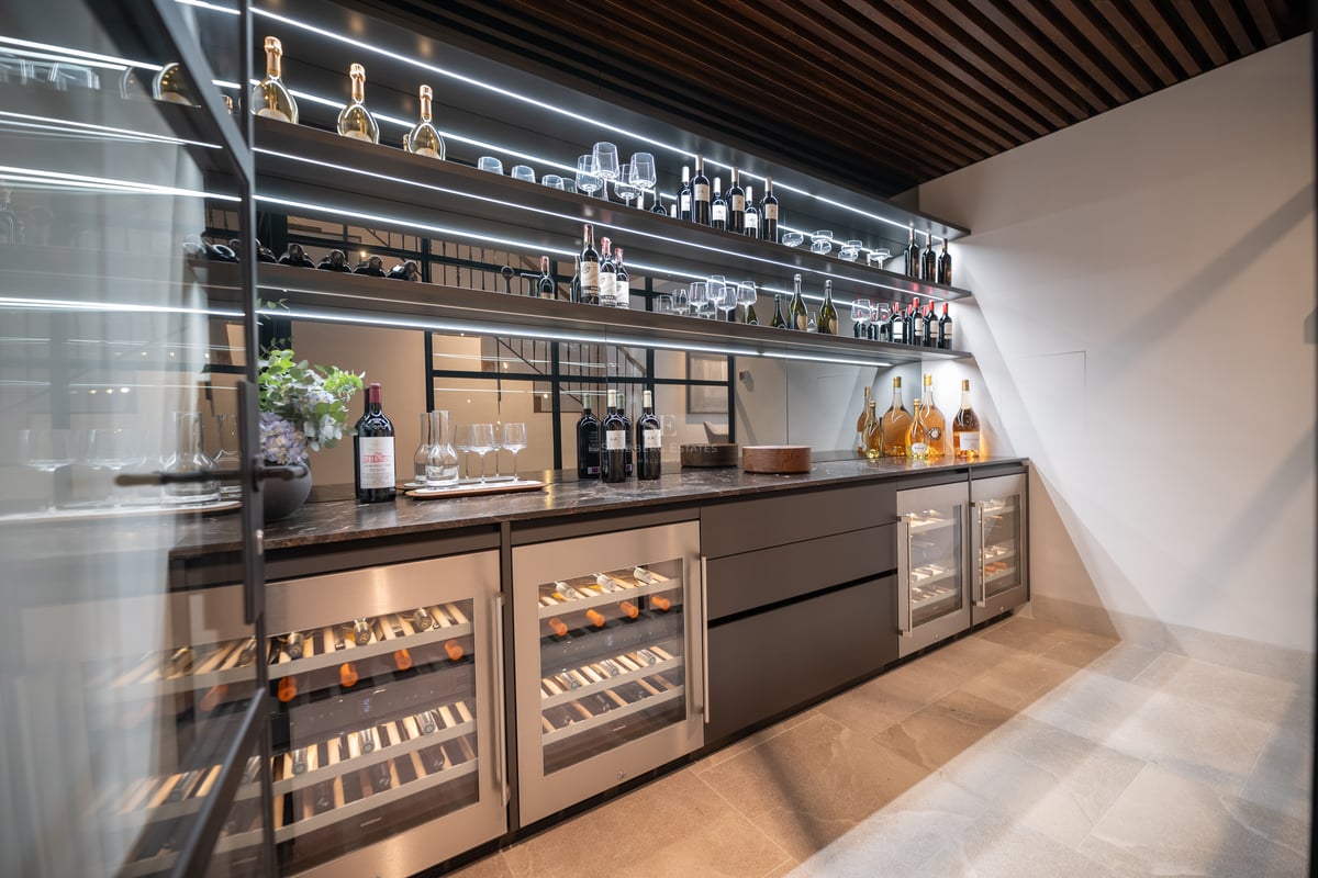 Cave à vin moderne avec refroidisseurs vitrés, étagères rétroéclairées et plans de travail en marbre sombre.