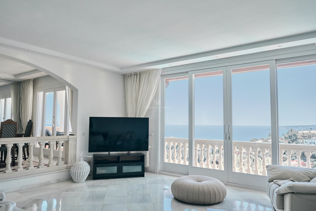 Salon lumineux avec sol en marbre blanc et grandes baies vitrées ouvrant sur une terrasse avec vue sur la mer.