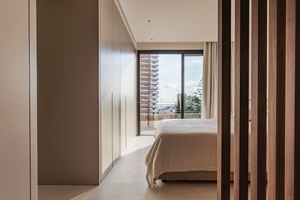 Chambre moderne avec placards intégrés, lit aux draps clairs et baie vitrée donnant sur la ville.