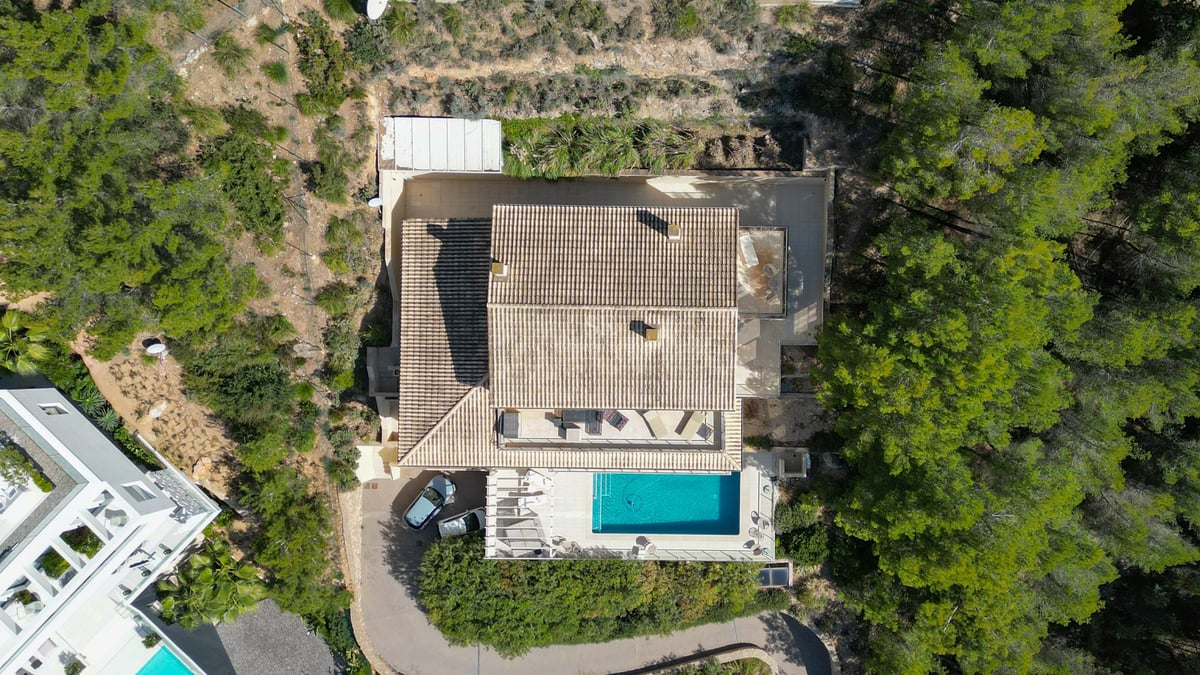 Vue aérienne d'une villa avec toit en tuiles, piscine et terrasses entourée d'une forêt de pins.