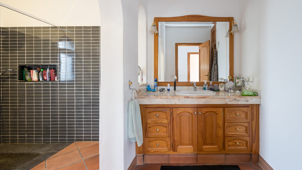 Salle de bain avec meuble en bois, plan en marbre, sol en terre cuite et douche à l'italienne grise.