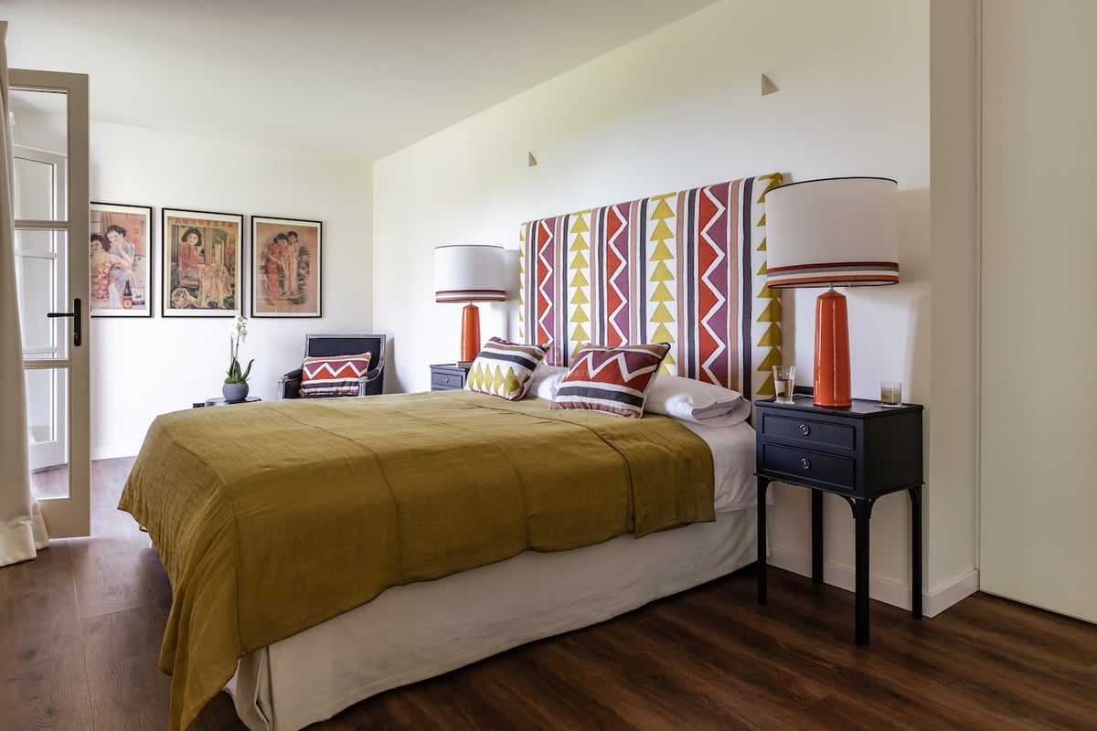 Chambre avec tête de lit géométrique, couvre-lit moutarde et lampes en céramique orange sur tables de chevet noires.