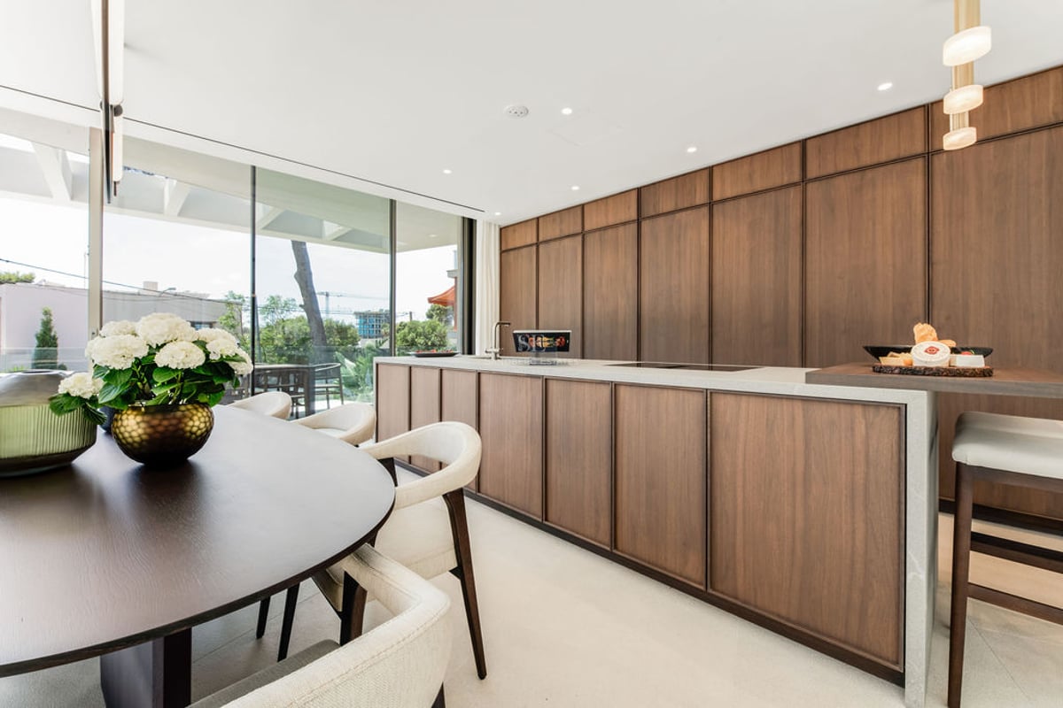 Cuisine moderne avec îlot central en bois sombre, plans de travail en pierre et coin repas près de grandes baies vitrées.