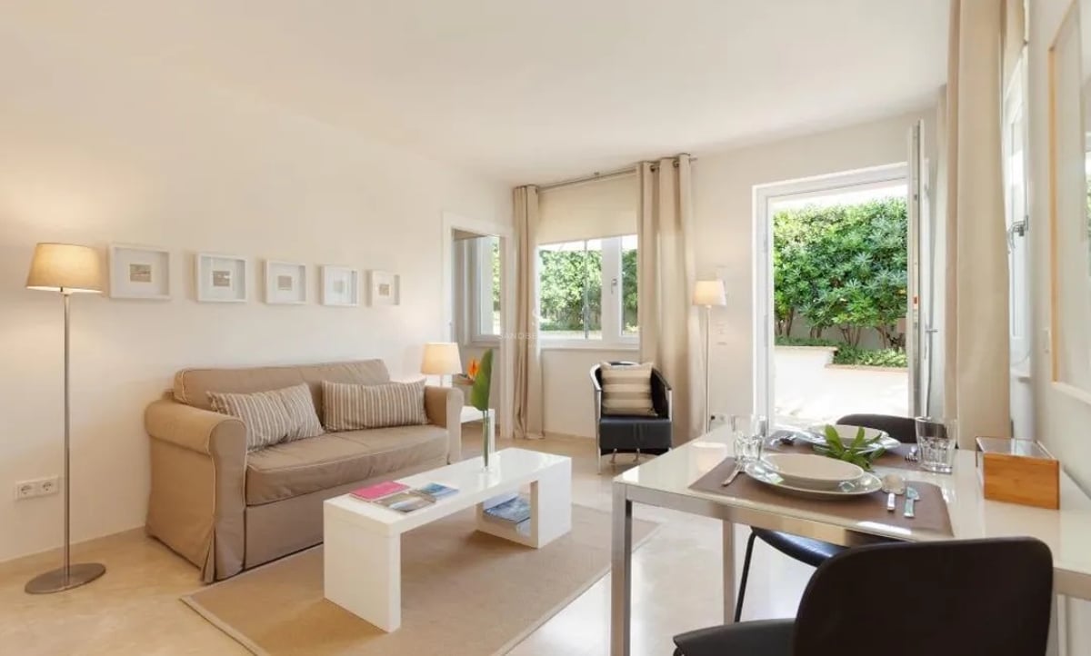 Salon contemporain aux tons crème avec coin repas s'ouvrant sur un jardin luxuriant.