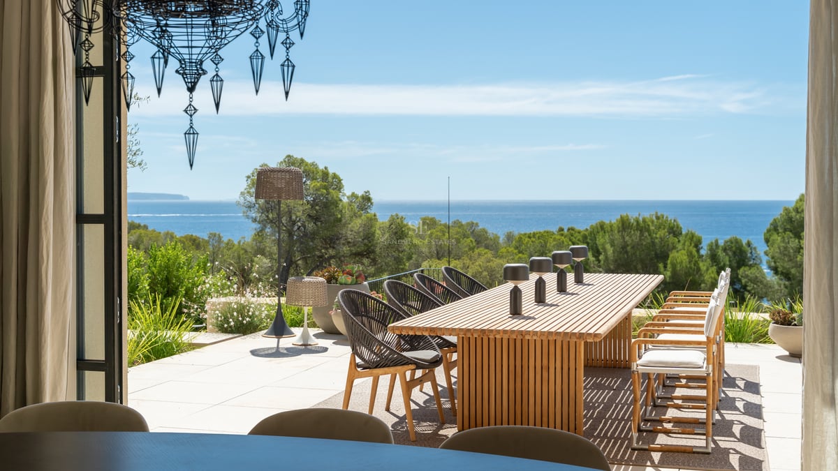 Table à manger extérieure en bois sur une terrasse surplombant une forêt de pins et la mer Méditerranée.