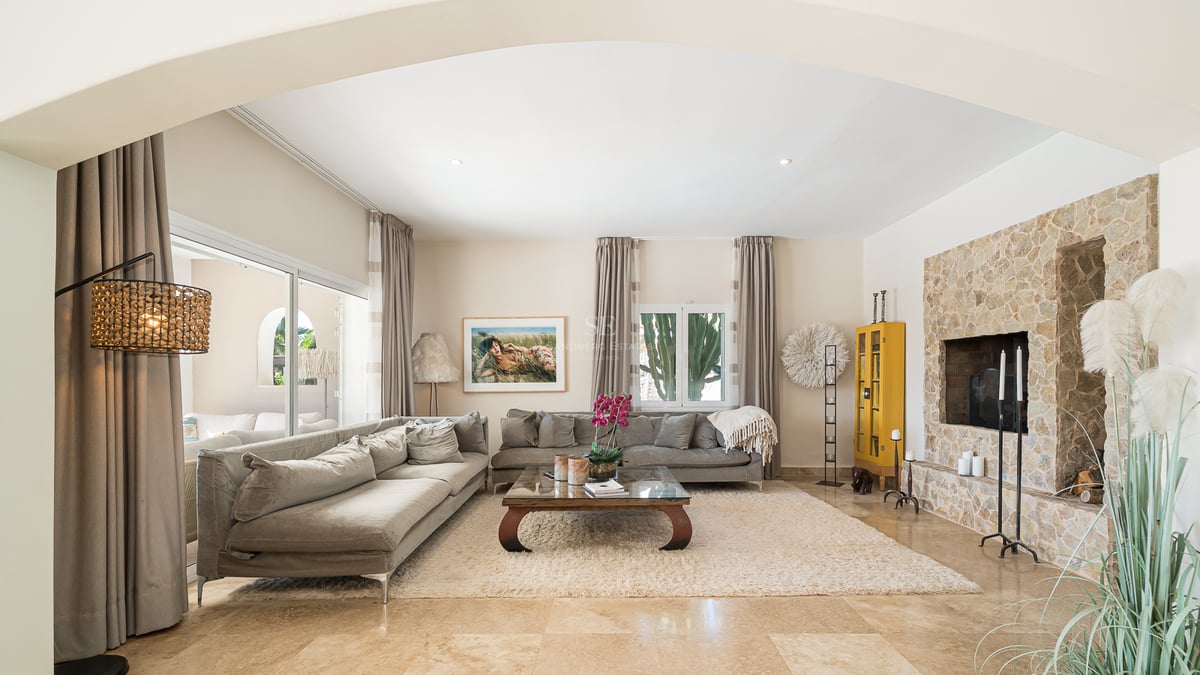 Salon spacieux avec canapés gris, tapis beige et un grand mur de cheminée en pierre naturelle.