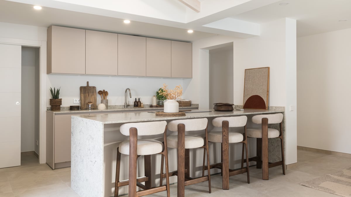 Cuisine contemporaine avec placards beiges, îlot en pierre blanche et quatre tabourets en bois et tissu.