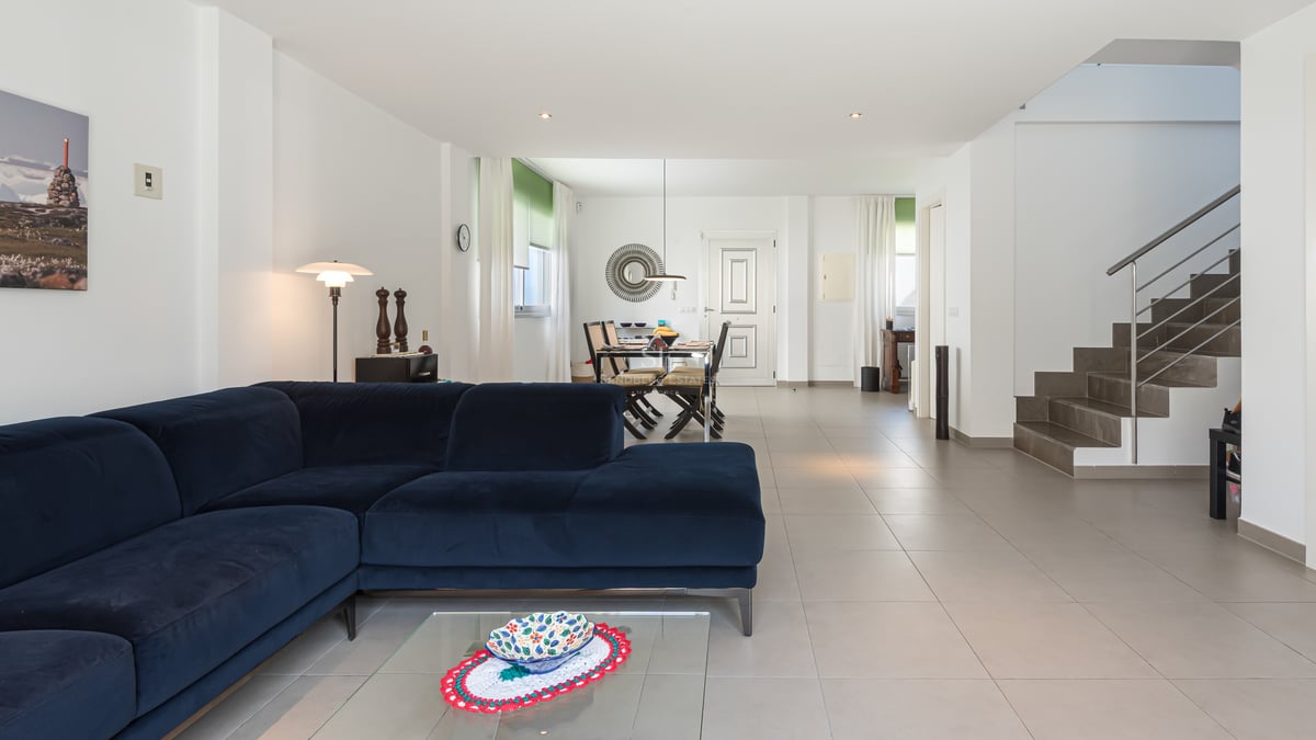 Salon lumineux avec canapé en velours bleu marine, sol en carrelage grand format et escalier vers l'étage.
