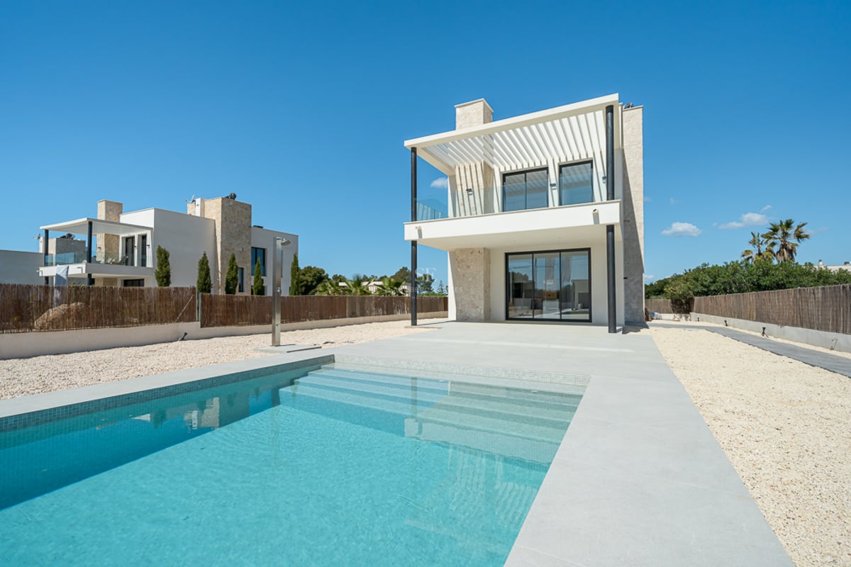 Piscine d'un bleu limpide avec marches, à côté d'une villa moderne de deux étages en blanc et pierre sous un ciel bleu.