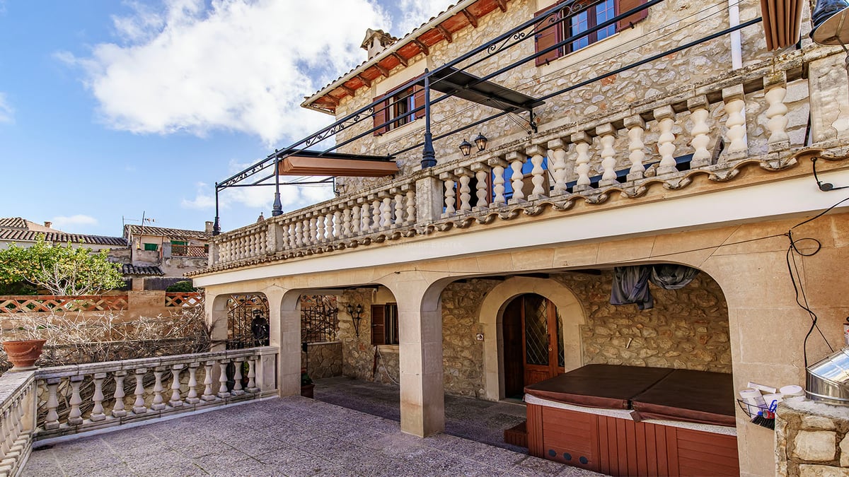 Façade en pierre sur deux niveaux avec porche voûté, terrasse à balustrade et bain à remous extérieur.