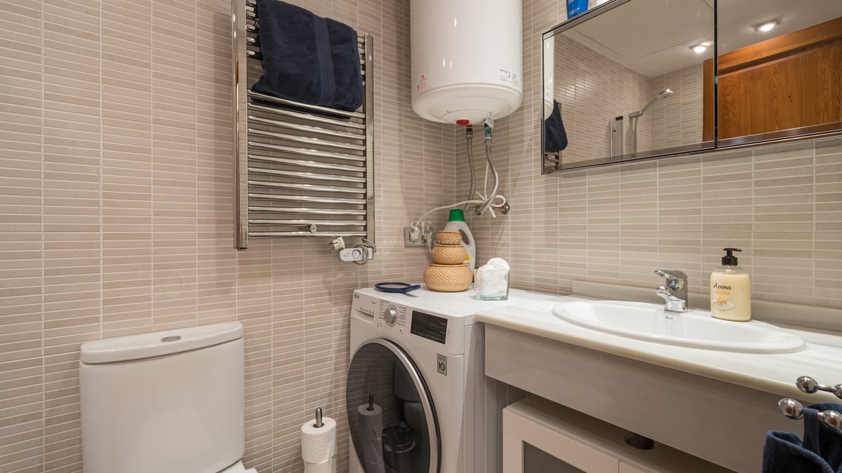 Salle de bains carrelée beige avec plan vasque en marbre, lave-linge et sèche-serviettes chauffant.