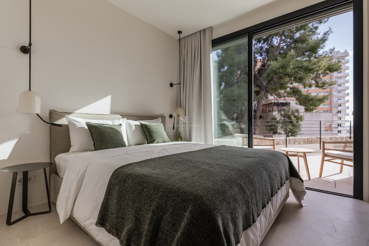 Chambre lumineuse avec lit double, coussins verts et grandes baies vitrées coulissantes ouvrant sur une terrasse.