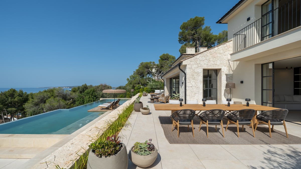 Terrasse de luxe avec piscine à débordement vue mer, salle à manger extérieure et façade en pierre naturelle.