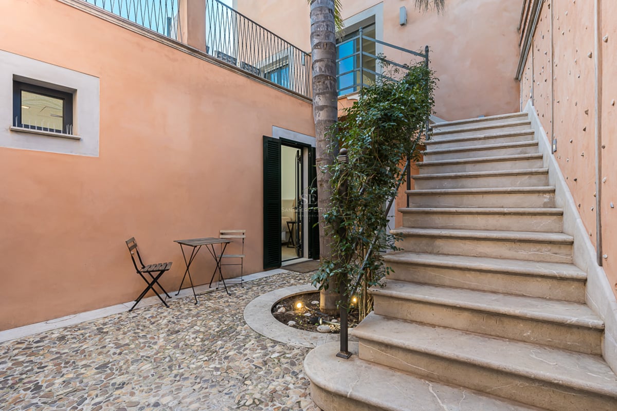 Cour privée aux murs pêche, sol en galets, escalier en pierre et table de bistrot.