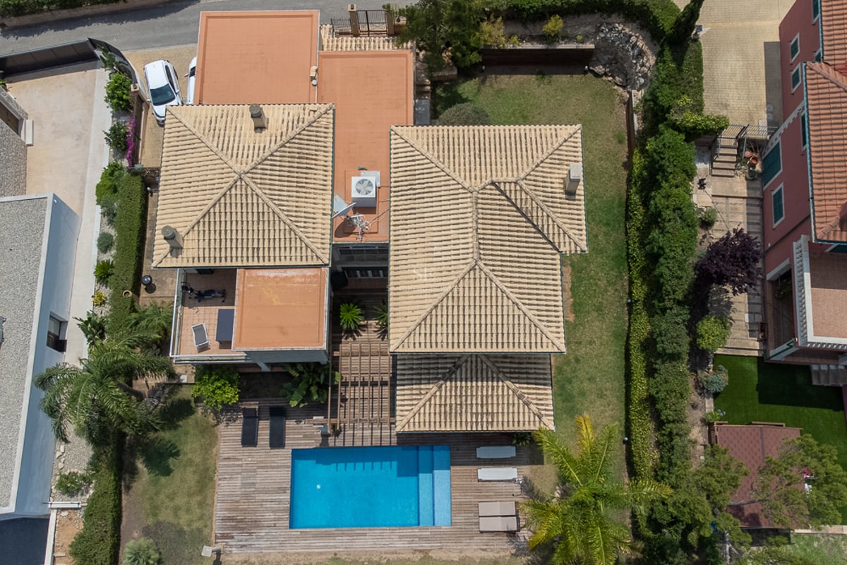 Vue de dessus d'une villa aux toits de tuiles beiges, piscine rectangulaire bleue et terrasse en bois avec jardin.