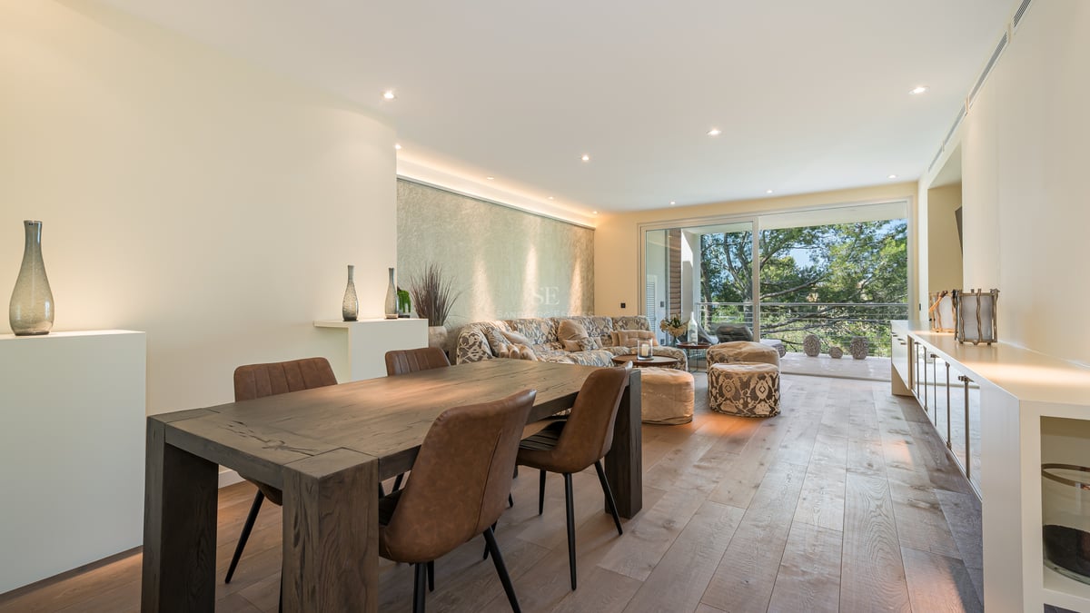 Espace de vie ouvert avec parquet en chêne, table en bois foncé et accès direct à une terrasse verdoyante.