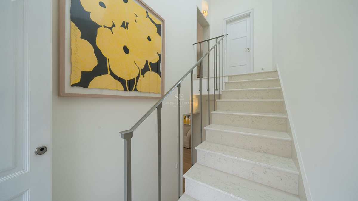 Escalier en pierre naturelle avec rampe fine en métal gris et tableau de fleurs jaunes sur mur blanc.