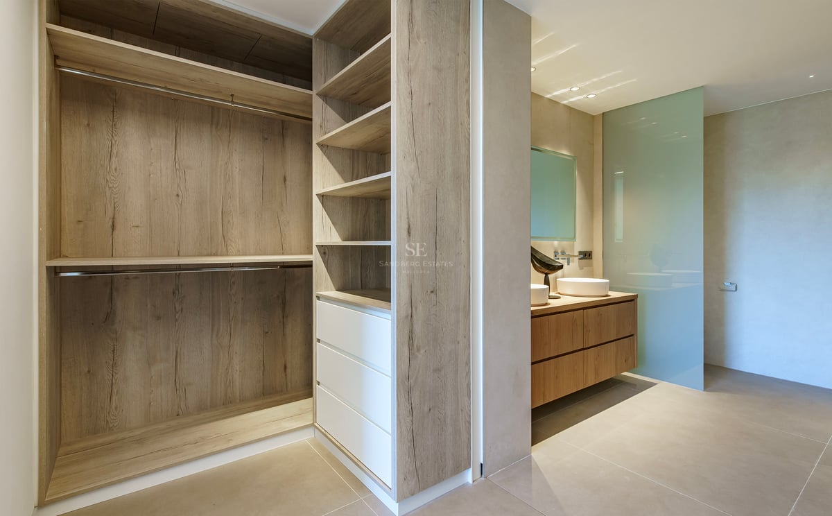 Dressing moderne avec menuiserie en chêne menant à une salle de bains avec double vasque et paroi en verre dépoli.