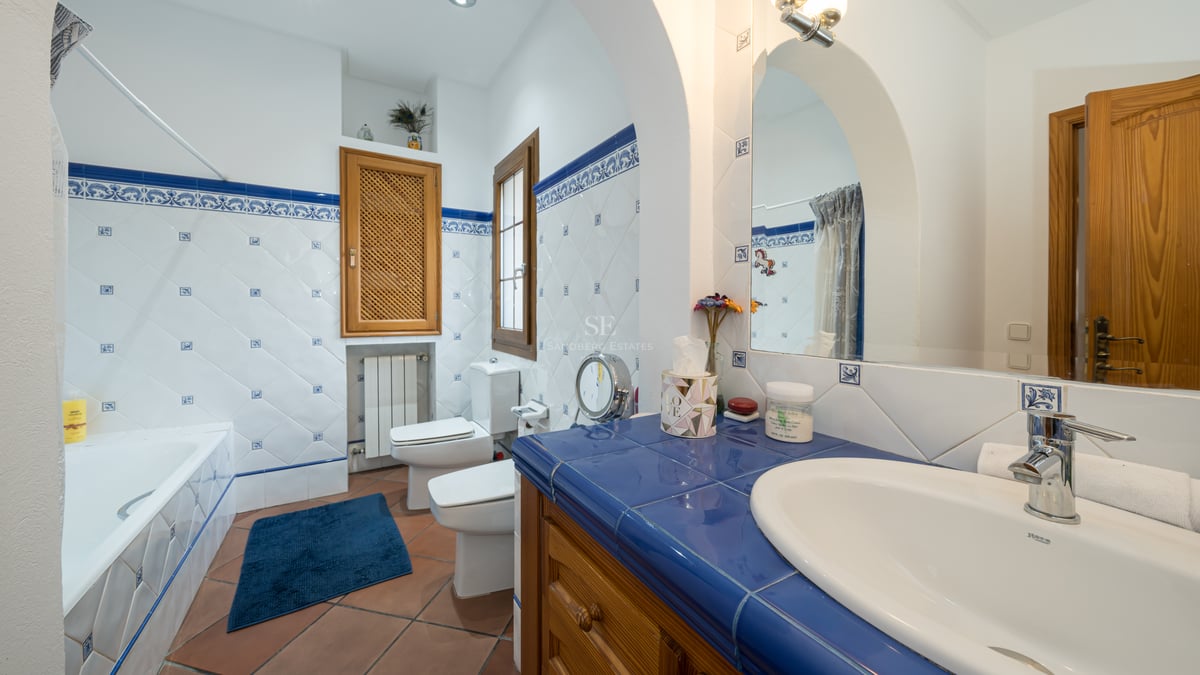 Salle de bains avec carrelage décoratif bleu et blanc, sol en terre cuite, meuble en bois et sanitaires blancs.