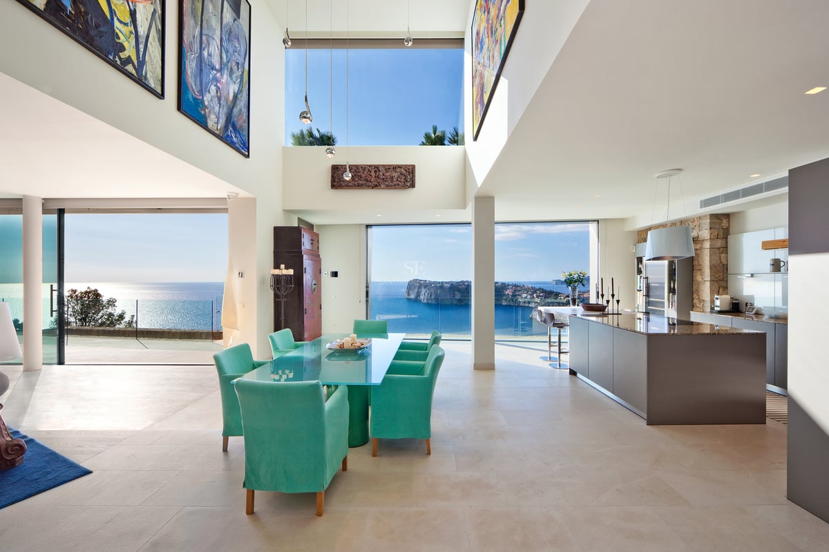 Salle à manger et cuisine modernes avec chaises turquoise et grandes baies vitrées offrant une vue mer panoramique.