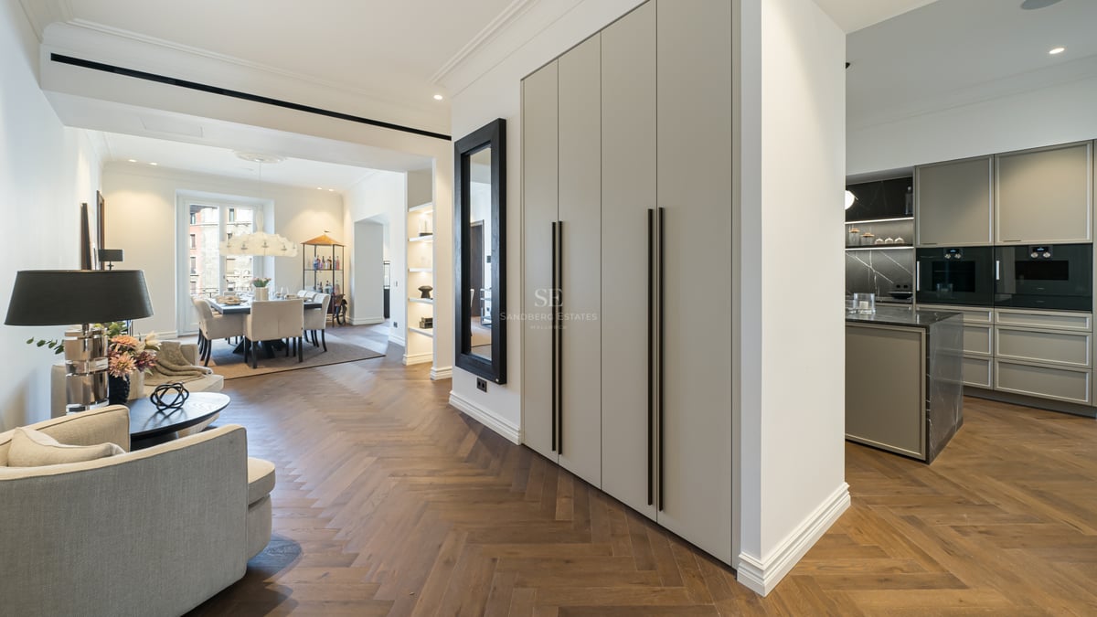 Modern open-plan apartment interior featuring oak herringbone floors, built-in storage, and a view of the dining area.