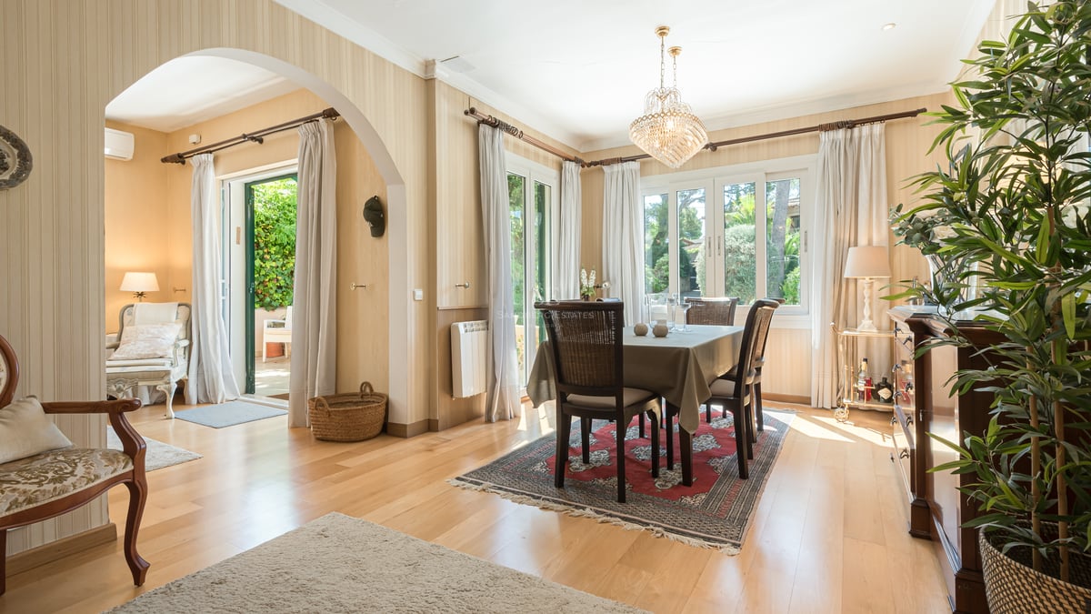 Salle à manger lumineuse avec lustre en cristal, meubles en bois sombre et portes-fenêtres ouvrant sur le jardin.