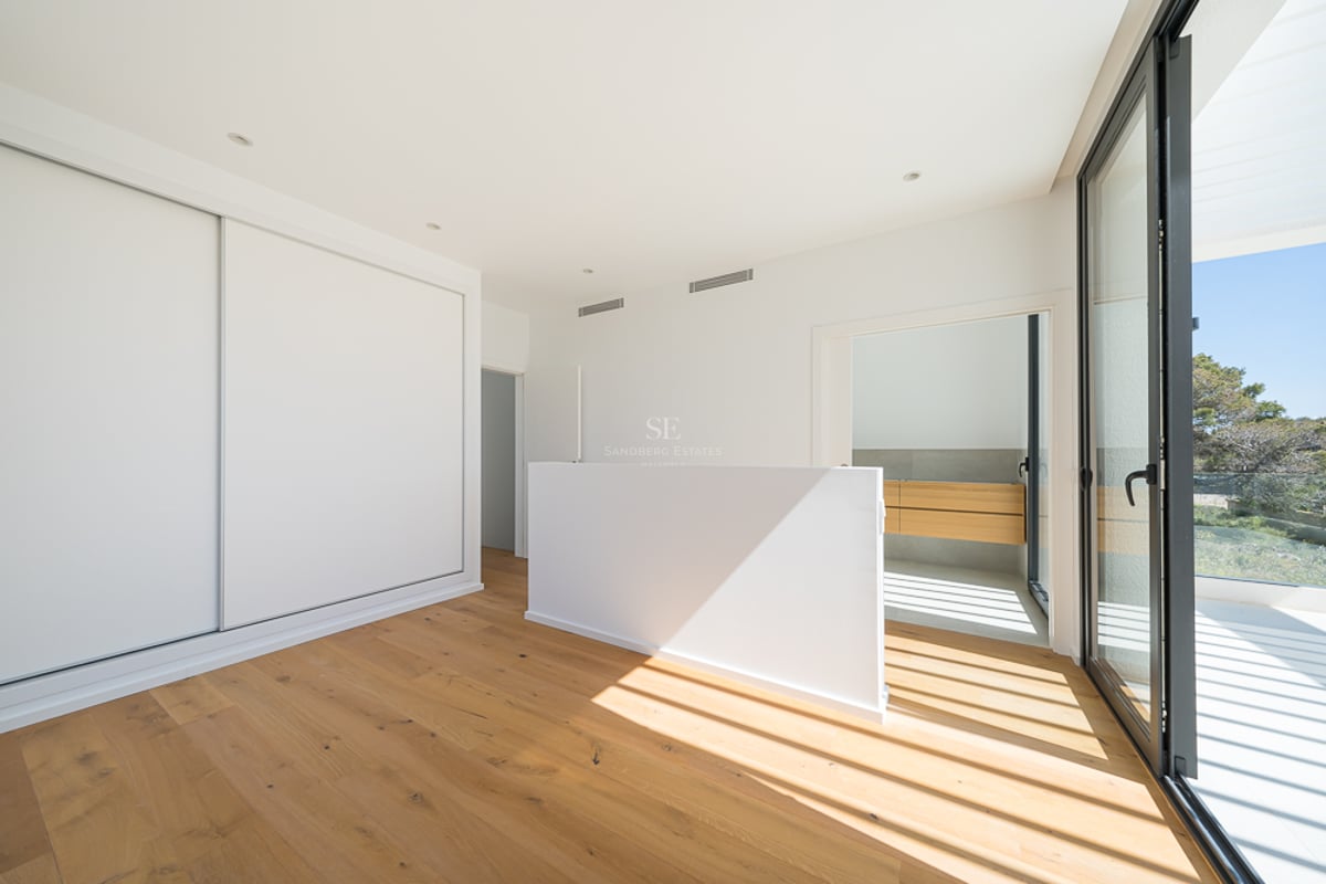 Chambre lumineuse avec parquet en chêne, placards blancs intégrés et grandes baies vitrées ouvrant sur une terrasse.