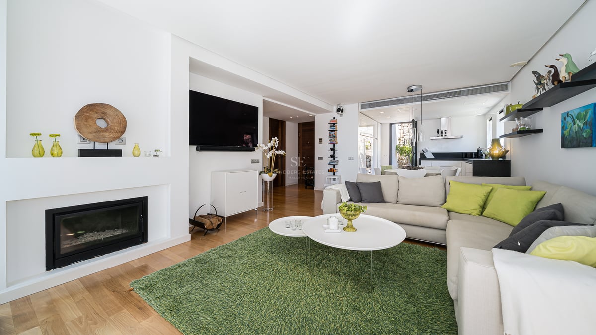 Salon lumineux avec parquet, canapé d'angle, cheminée intégrée et tapis vert dans un espace ouvert.